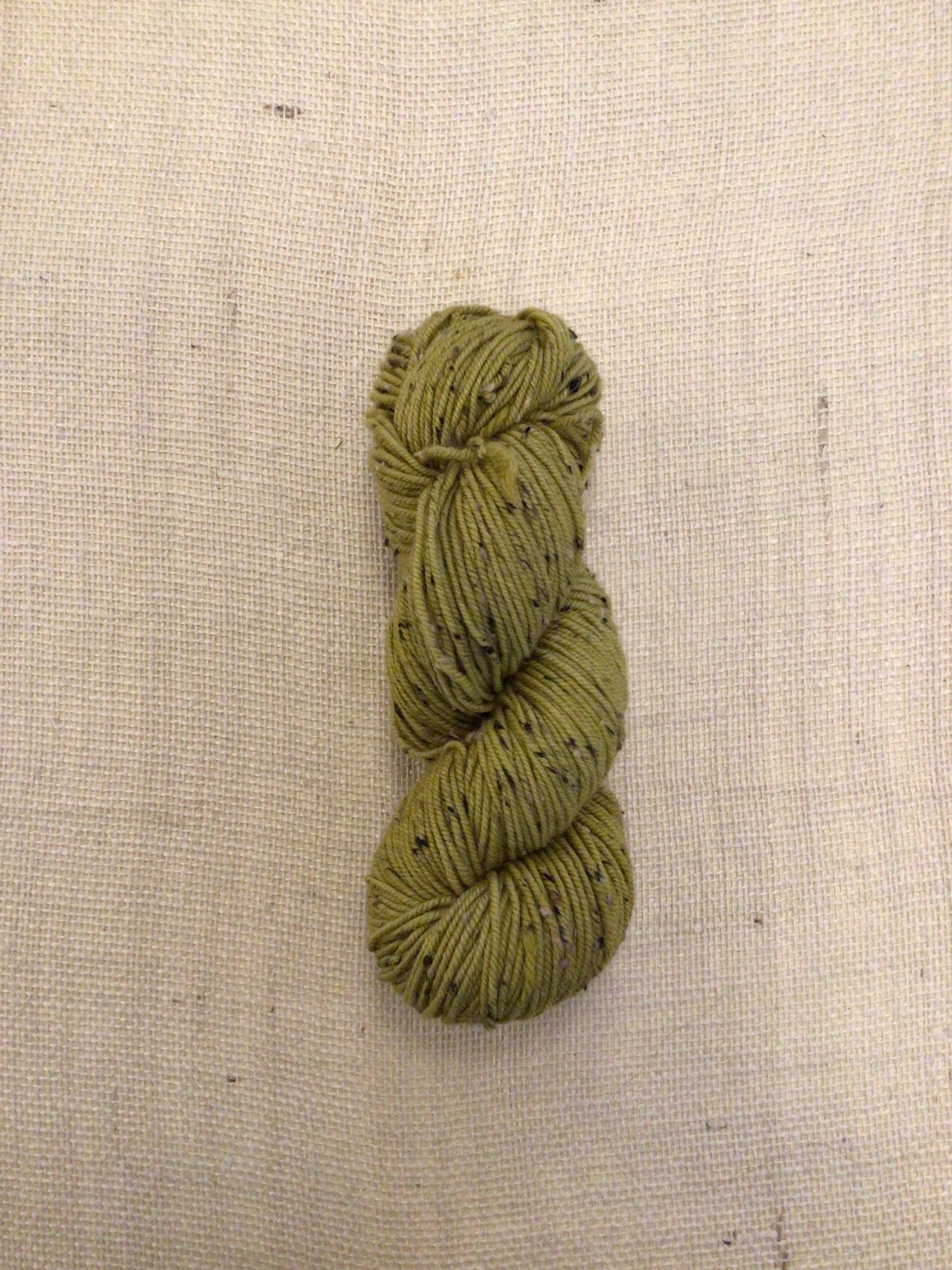 Willow green yarn with black and green specks on a beige background