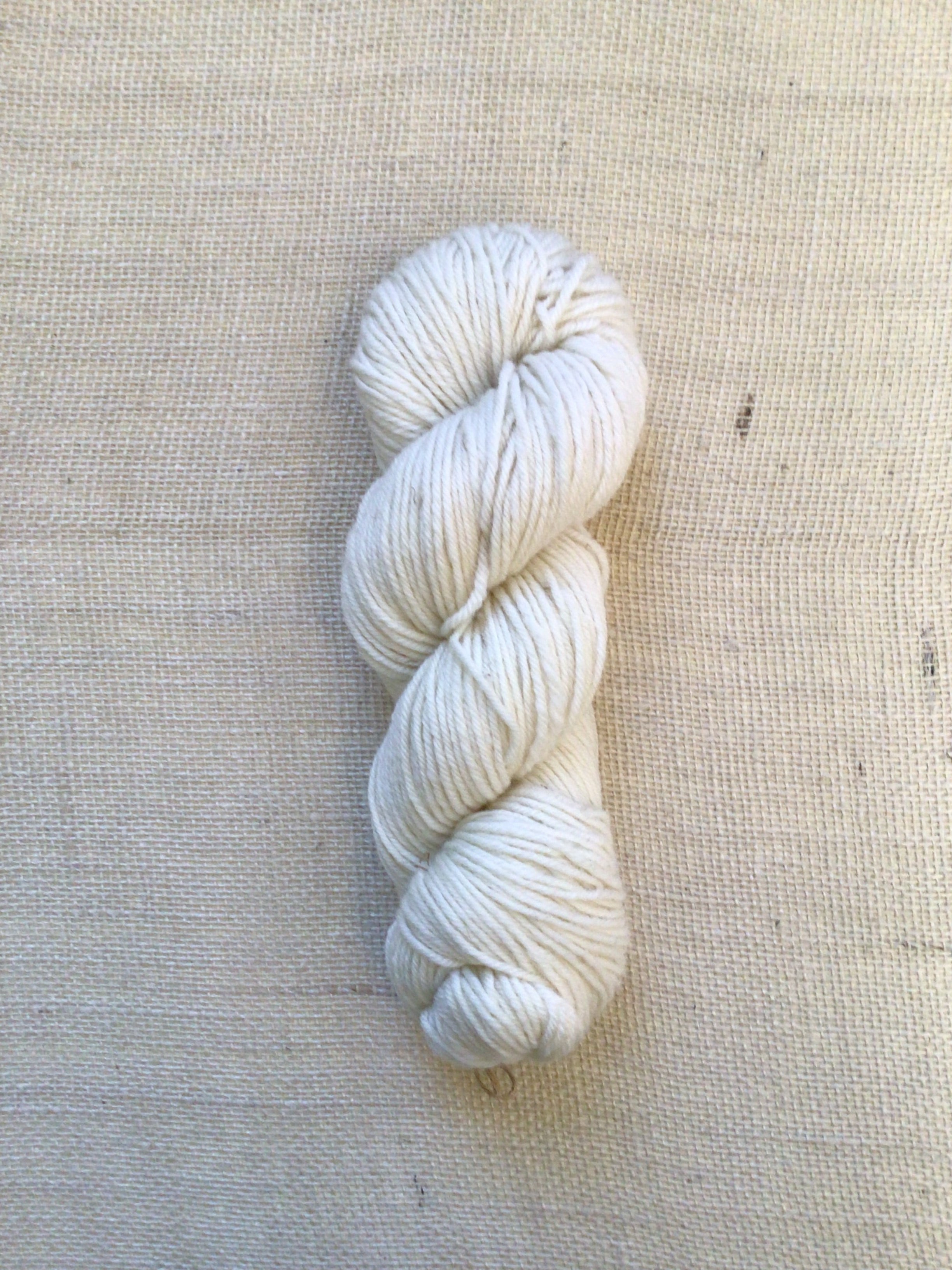 A skein of natural white yarn on a neutral canvas background