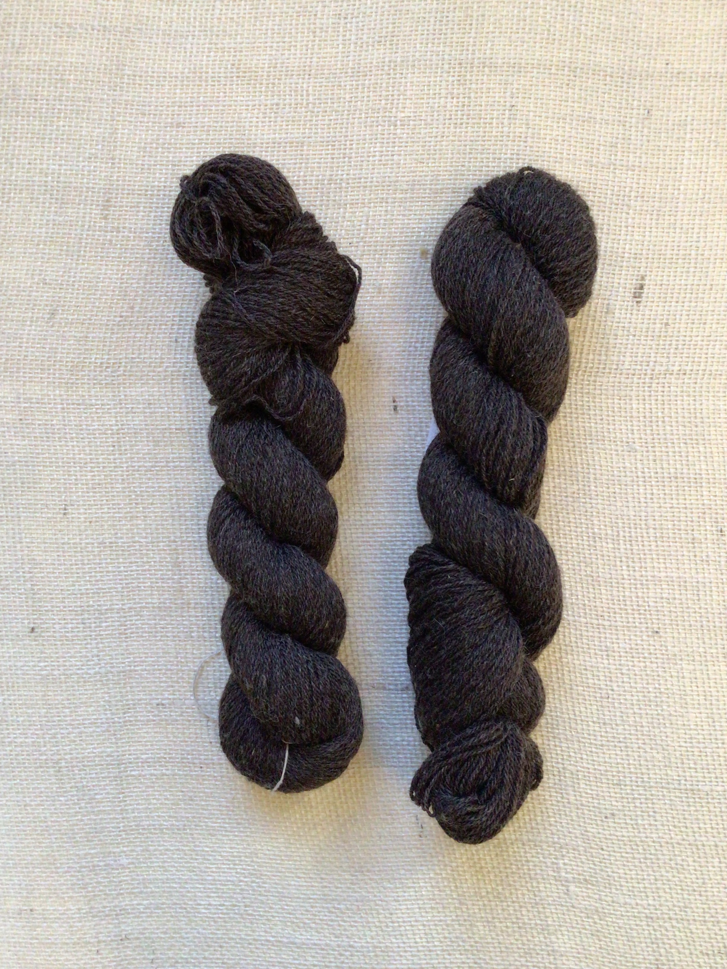 Two skeins of natural dark brown yarn in a neutral canvas background