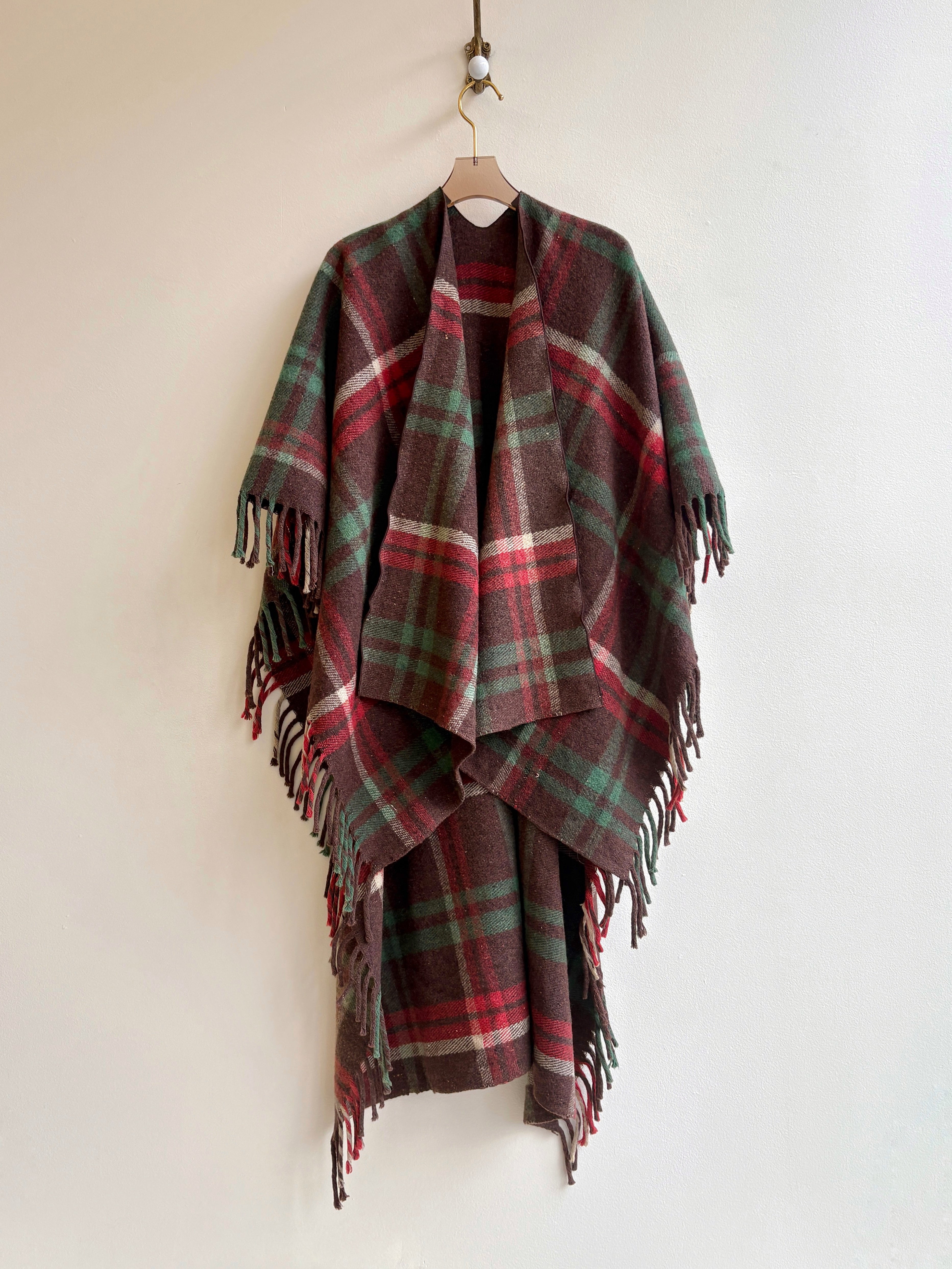 Plaid poncho with fringes on a hanger against a white background