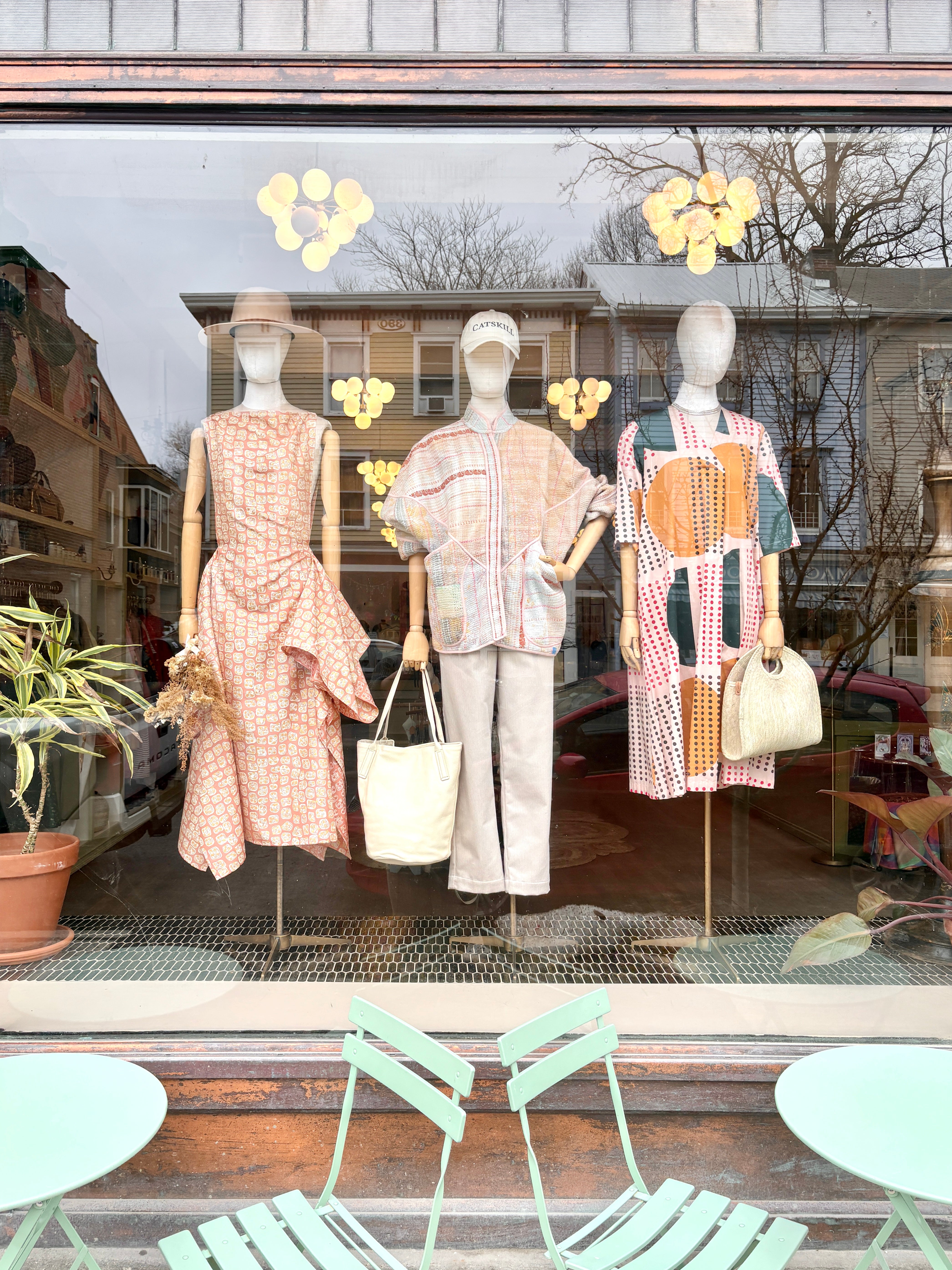 Mannequins in a store window display with clothing and bags, all in peach tones.